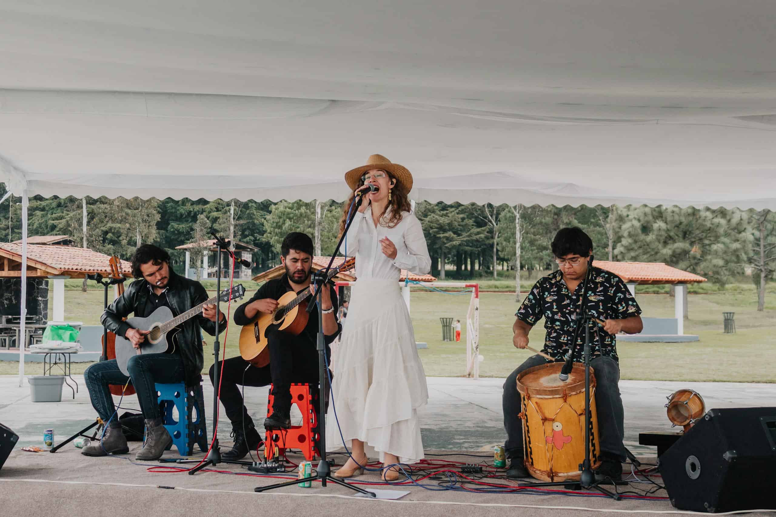 A musical band performing outdoors under a tent with instruments and a female singer.