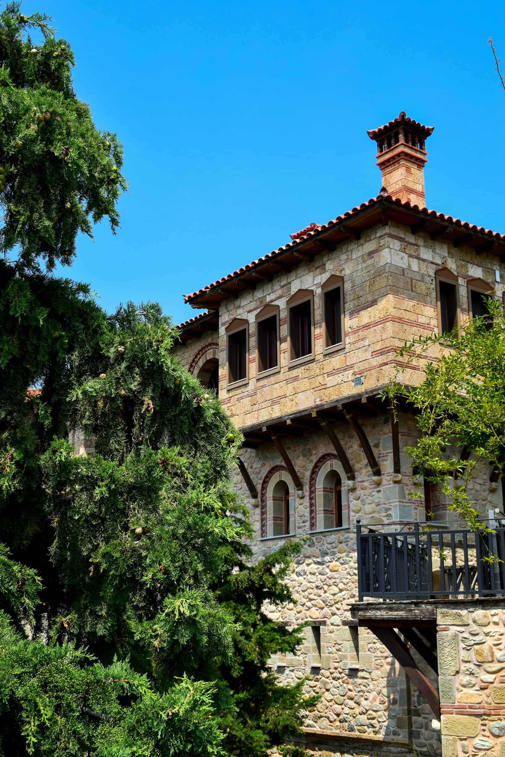 A scenic view of a historic Greek monastery surrounded by lush trees in Kalabaka, Greece.