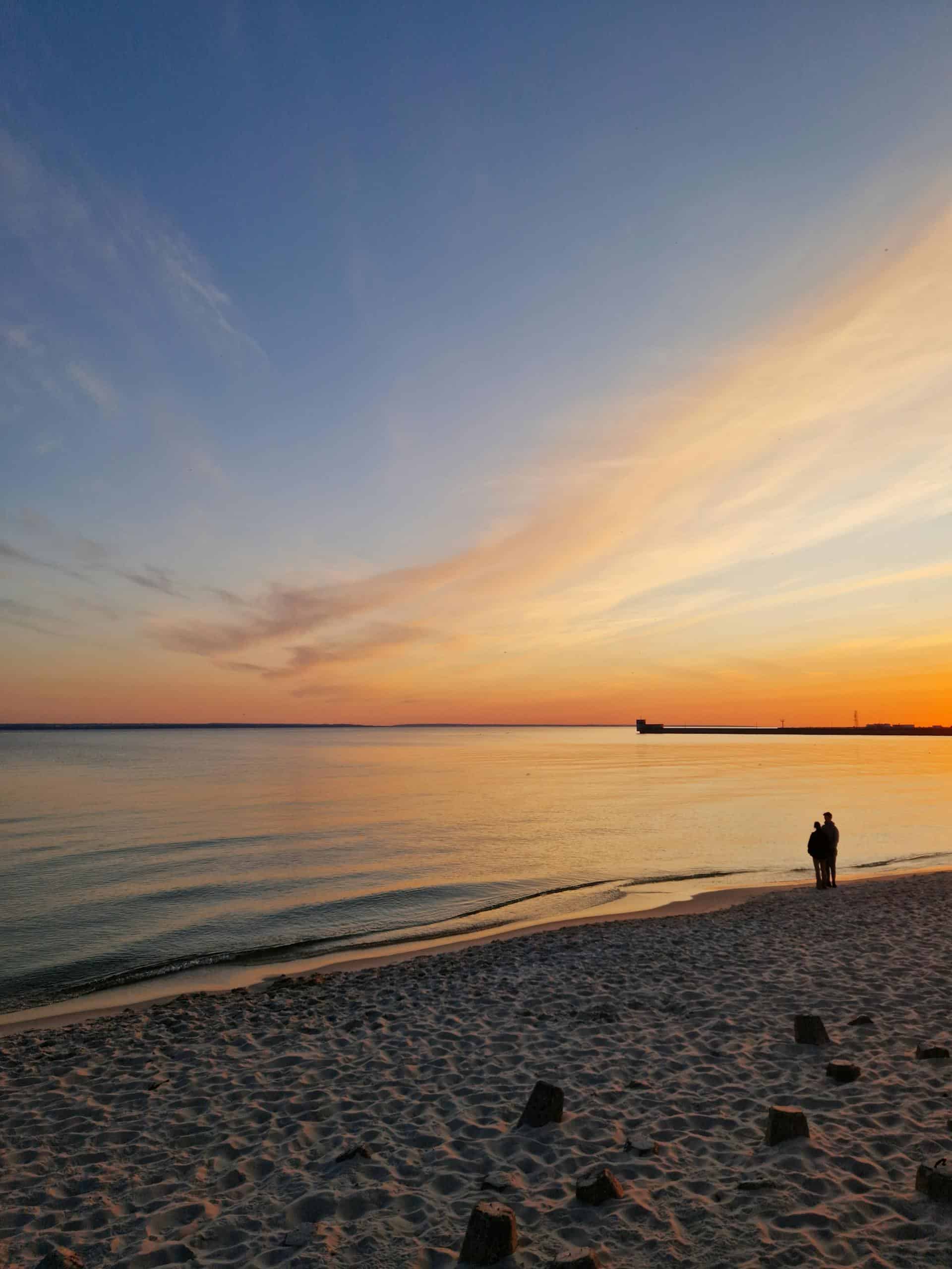 A serene sunset at Hel, Poland, with silhouettes on the beach and vibrant sky reflections.