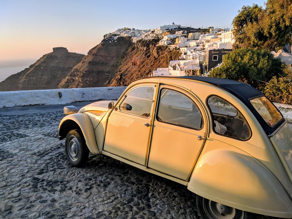 Classic vintage car parked with a stunning view of Santorini's iconic architecture at sunset.