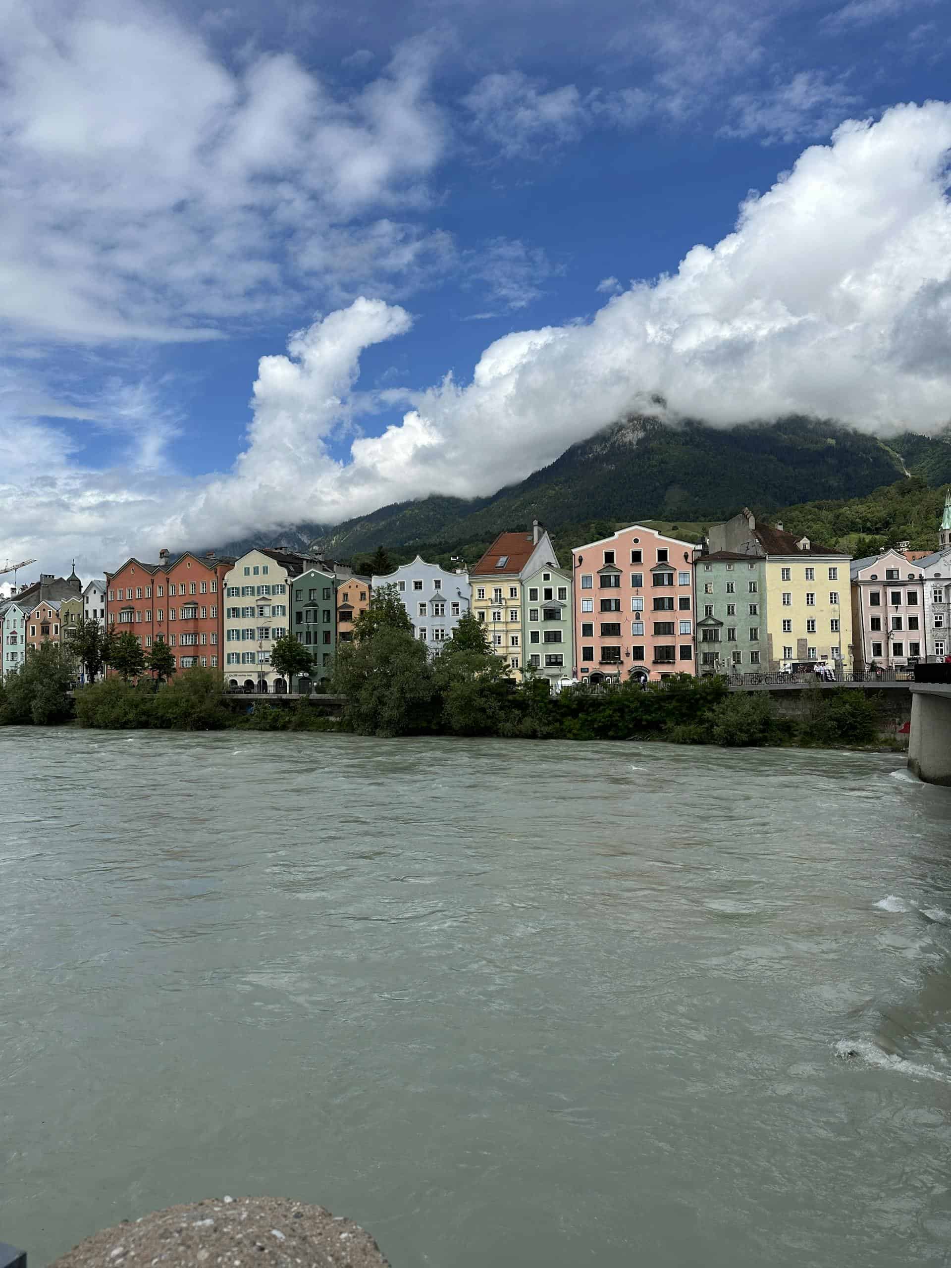 Scenic view of pastel-colored houses by the river in Innsbruck with mountains in the background.