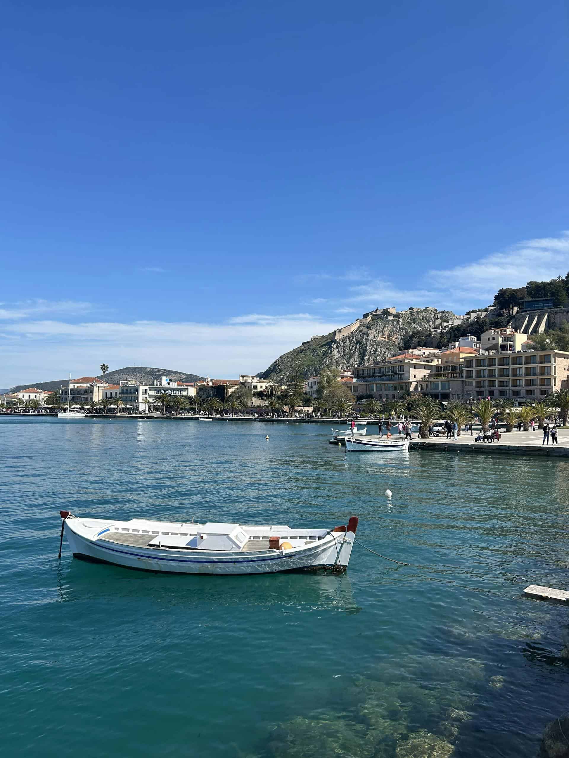Tranquil harbor scene in Nafplio featuring boats and historic architecture against a clear blue sky.