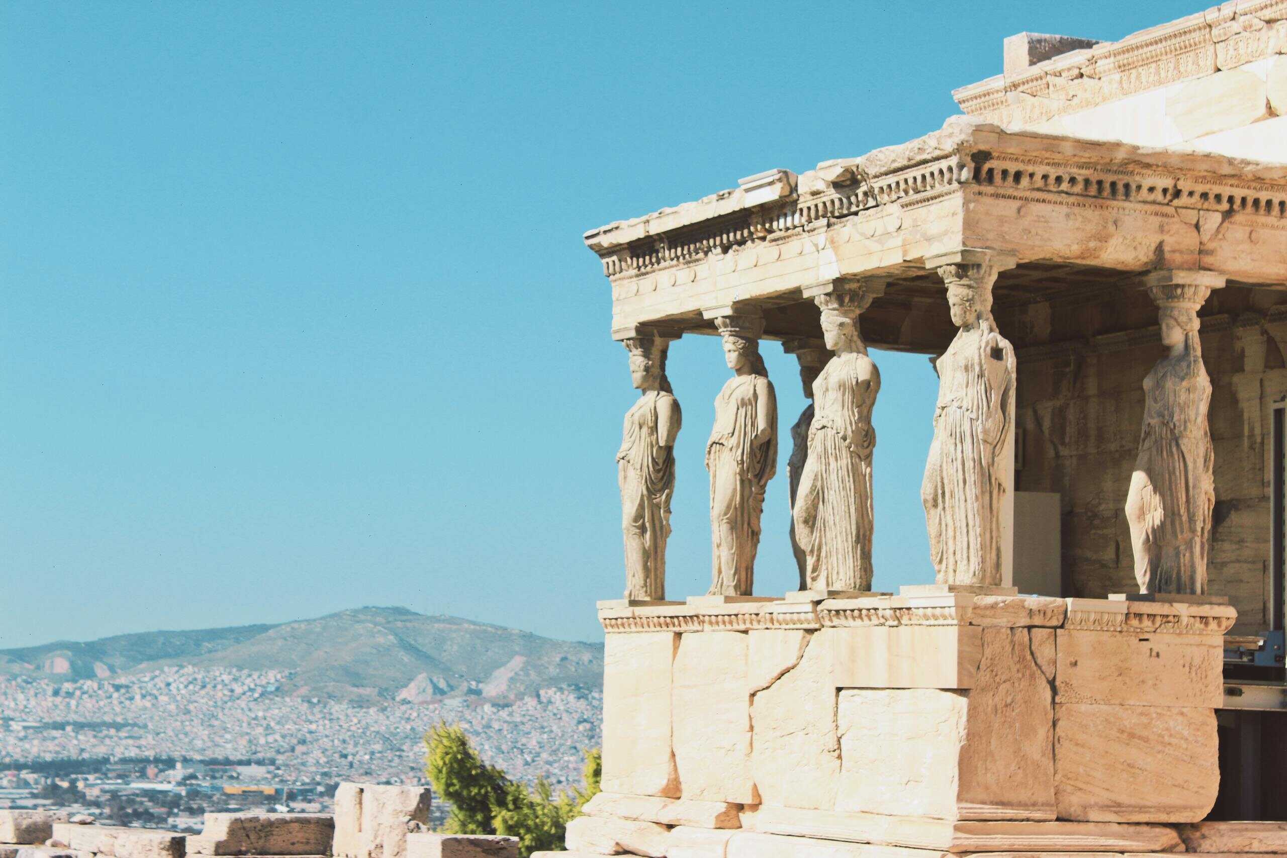 View of the Caryatids on the Erechtheion temple at the Acropolis in Athens under a clear blue sky.