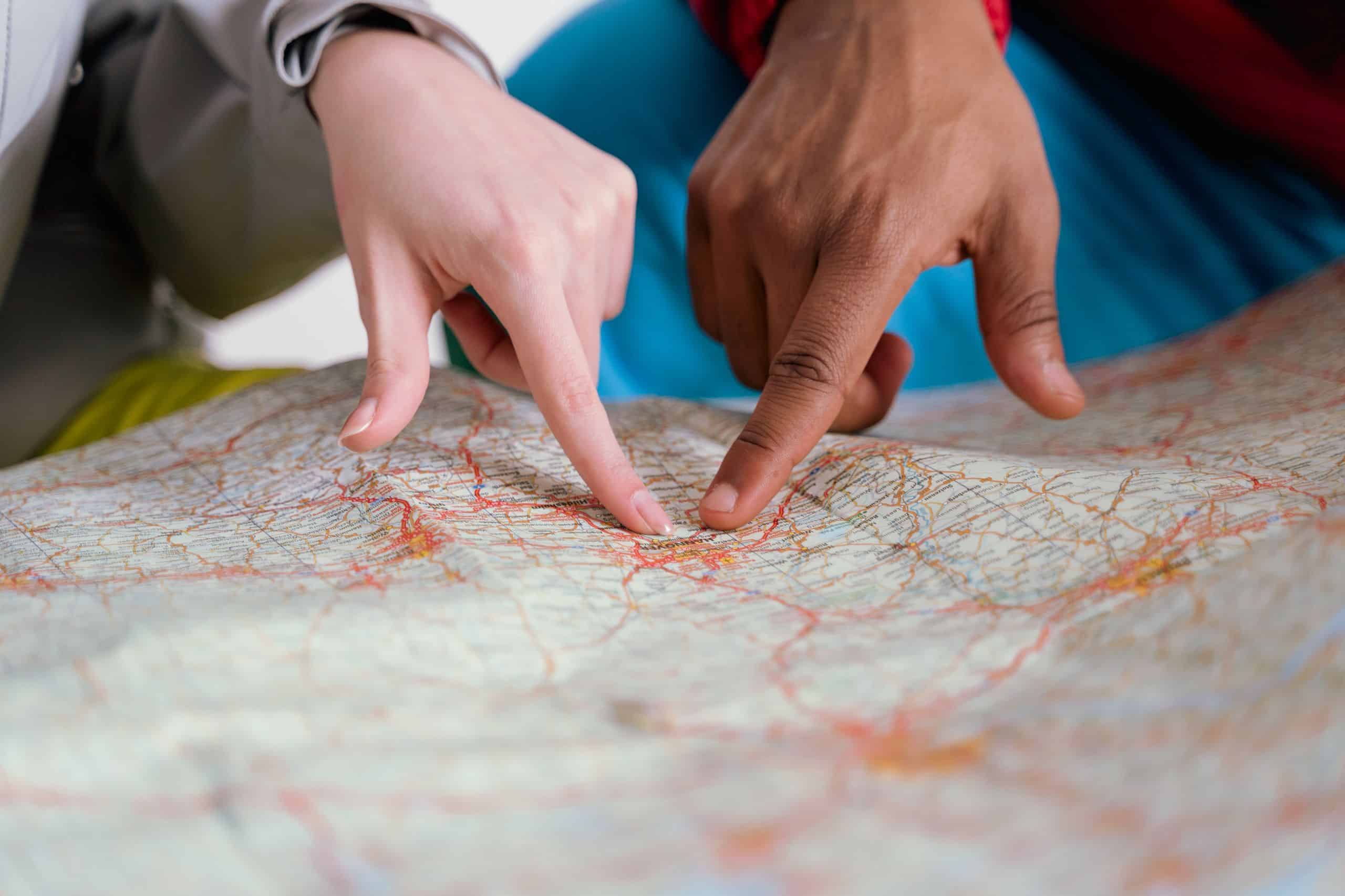 Close-up of diverse hands pointing at a paper map, symbolizing travel planning and navigation.